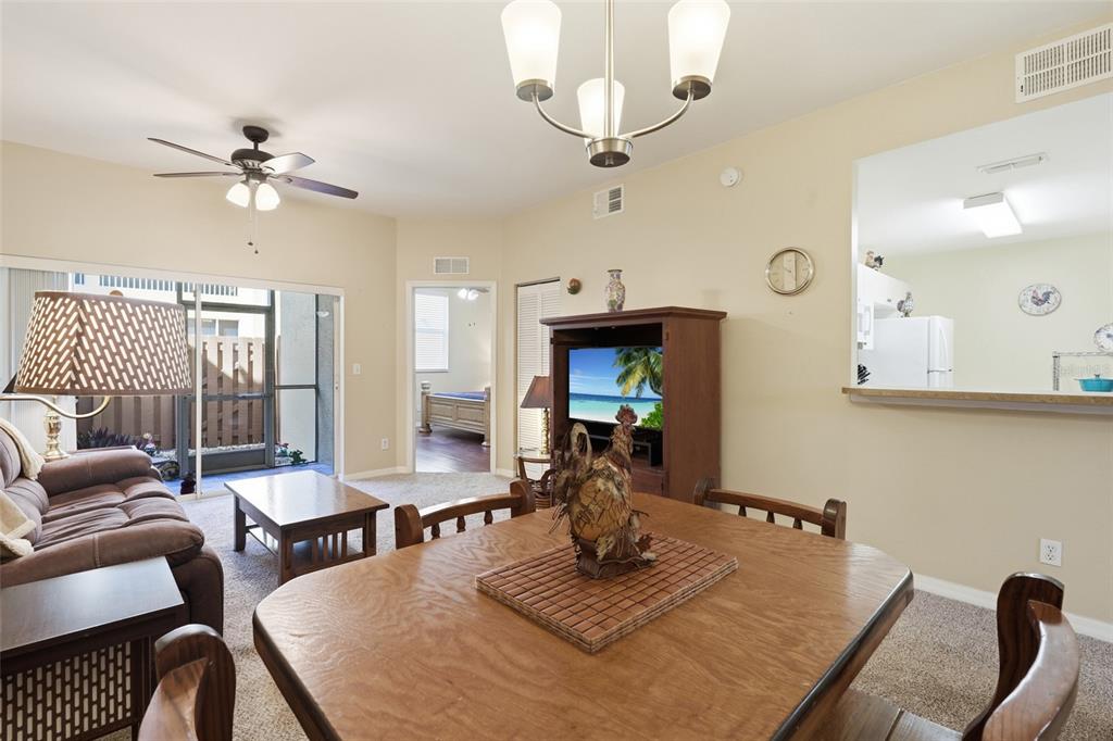 A dining area with a wooden table leads into a living room with a ceiling fan — 4259 BELLASOL CIRCLE UNIT 2013, FORT MYERS, FL