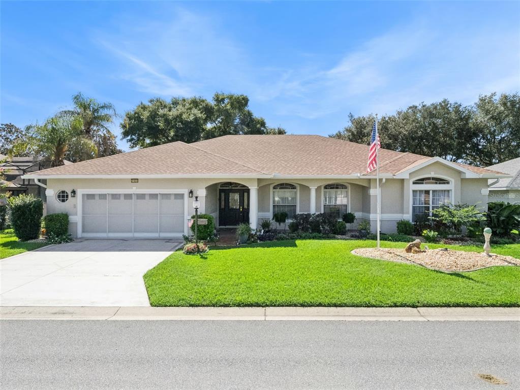 A single-story house with a two-car garage, a lawn, and an American flag — 21824 TARTAN STREET, LEESBURG, FL