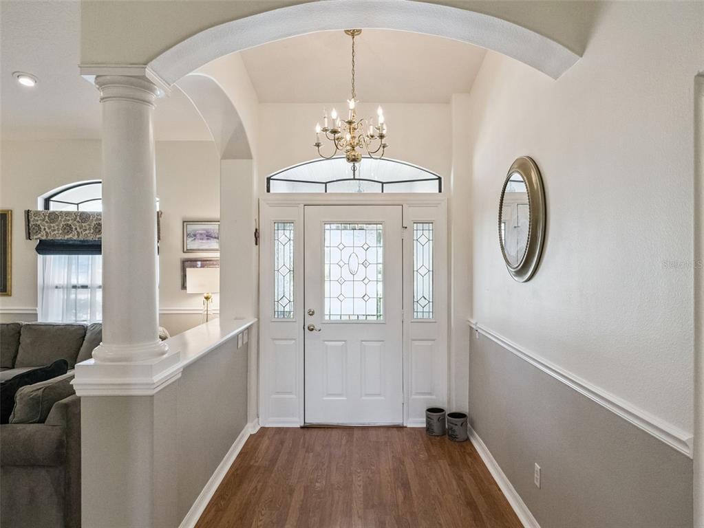 An entryway features a white front door with sidelights, a chandelier, and wood-look flooring — 21824 TARTAN STREET, LEESBURG, FL