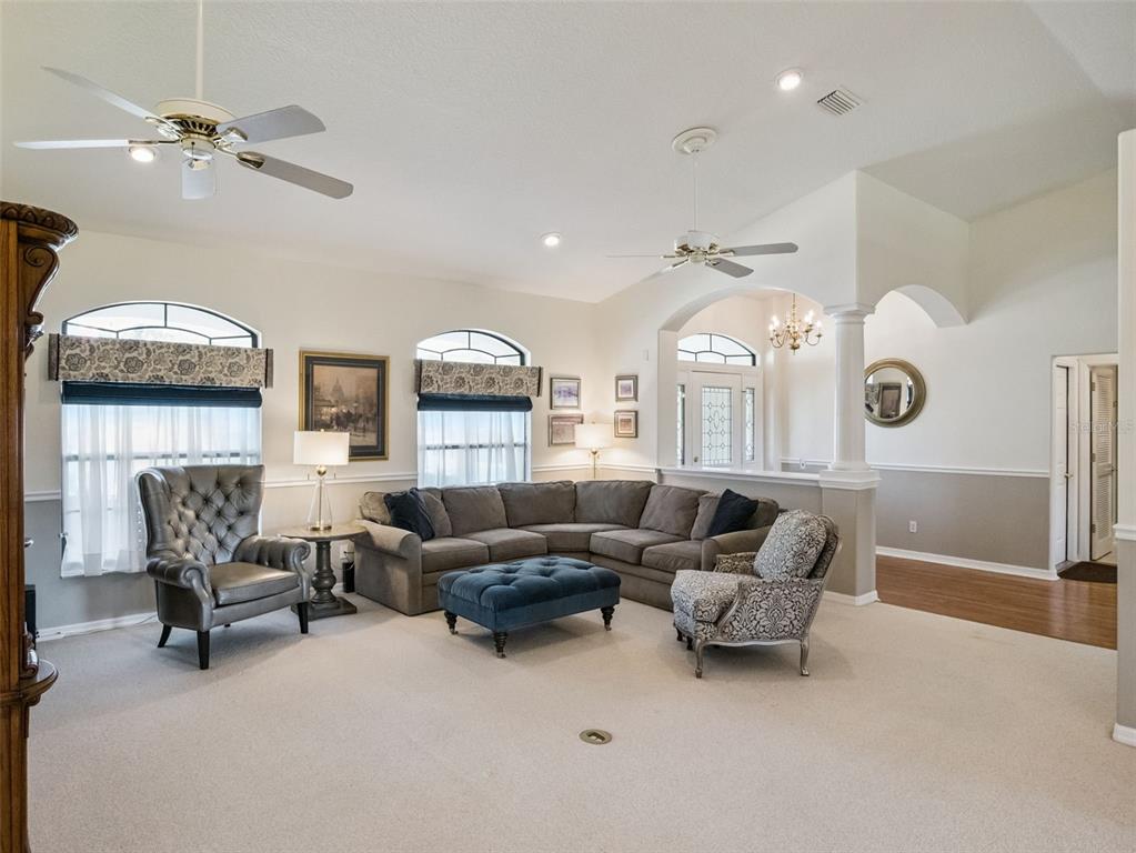 A living room features a sectional sofa, two armchairs, a blue ottoman, and ceiling fans — 21824 TARTAN STREET, LEESBURG, FL