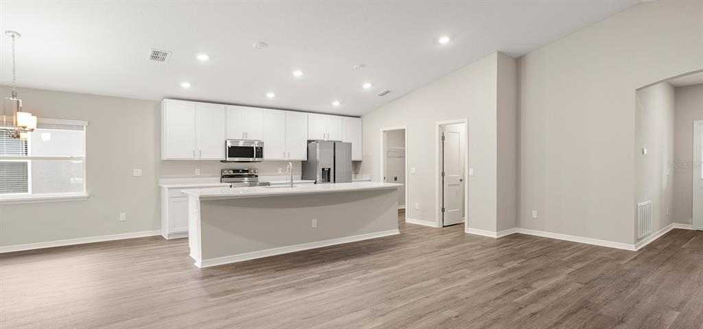 A modern kitchen features white cabinets, stainless steel appliances, and a large island with seating — 617 CYPRESS CREEK RUN, ST CLOUD, FL