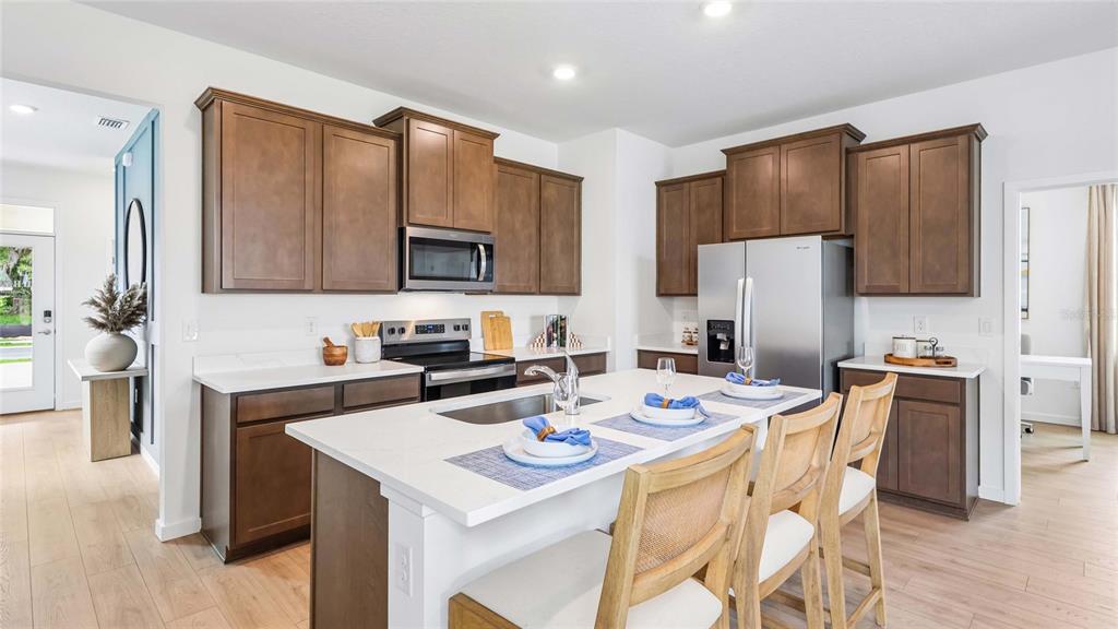 A kitchen with brown cabinets, a white island, stainless steel appliances, and light wood flooring — 8782 PINECREST TRAIL, WILDWOOD, FL