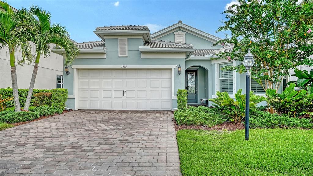 A light blue single-story house features a paved driveway, a two-car garage, and landscaped gardens — 3355 ANCHOR BAY TRAIL, BRADENTON, FL
