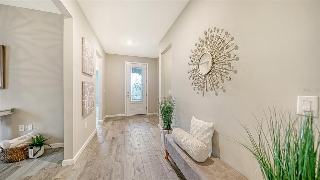 A bright entryway features light wood-look tile flooring, a sunburst mirror, and a small bench — 3355 ANCHOR BAY TRAIL, BRADENTON, FL