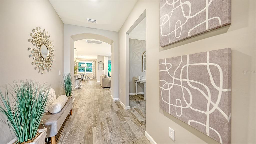 A hallway with wood-look tile flooring leads to an open-concept living area and kitchen — 3355 ANCHOR BAY TRAIL, BRADENTON, FL