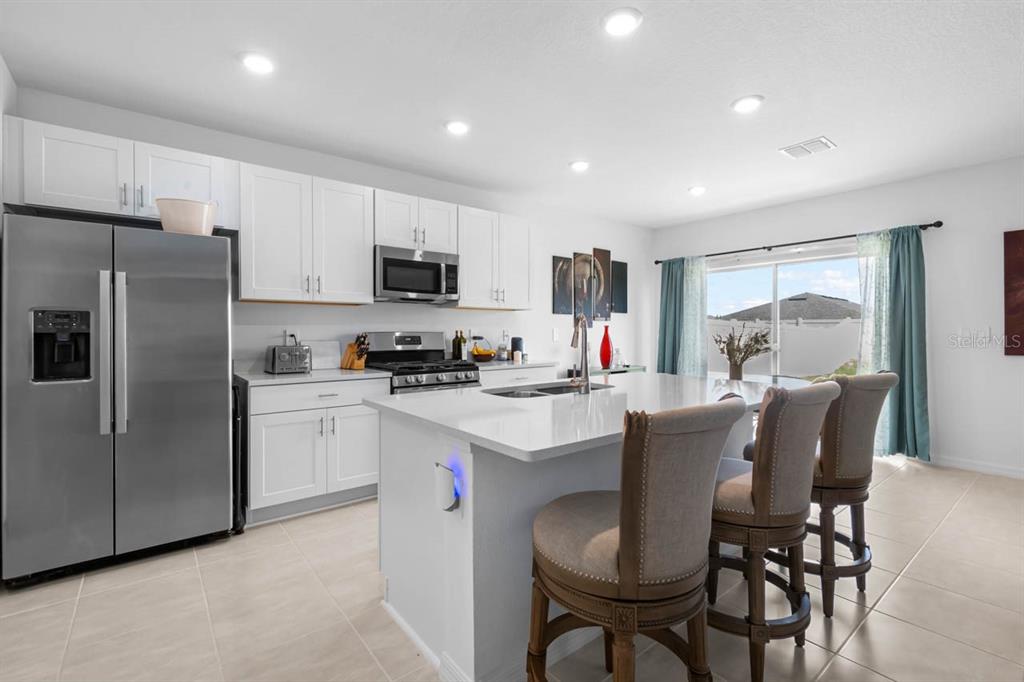 A modern kitchen features white cabinets, stainless steel appliances, a large island, and bar stools — 13524 CAMELOT CT, PARRISH, FL