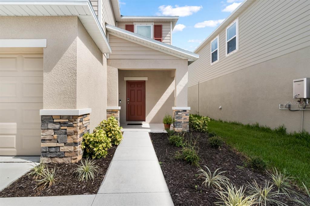 A beige house exterior features a stone-accented garage, a red front door, and a walkway — 13524 CAMELOT CT, PARRISH, FL