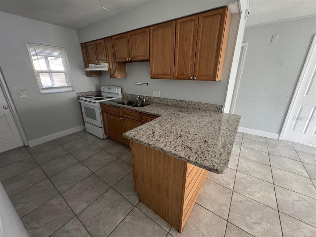 A kitchen features light wood cabinets, granite countertops, a white stove, and tiled flooring — 1392 KING STREET UNIT 1394, BARTOW, FL