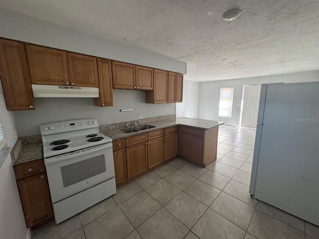 A kitchen features wood cabinets, granite countertops, a white stove, and light-colored floor tiles — 1392 KING STREET UNIT 1394, BARTOW, FL