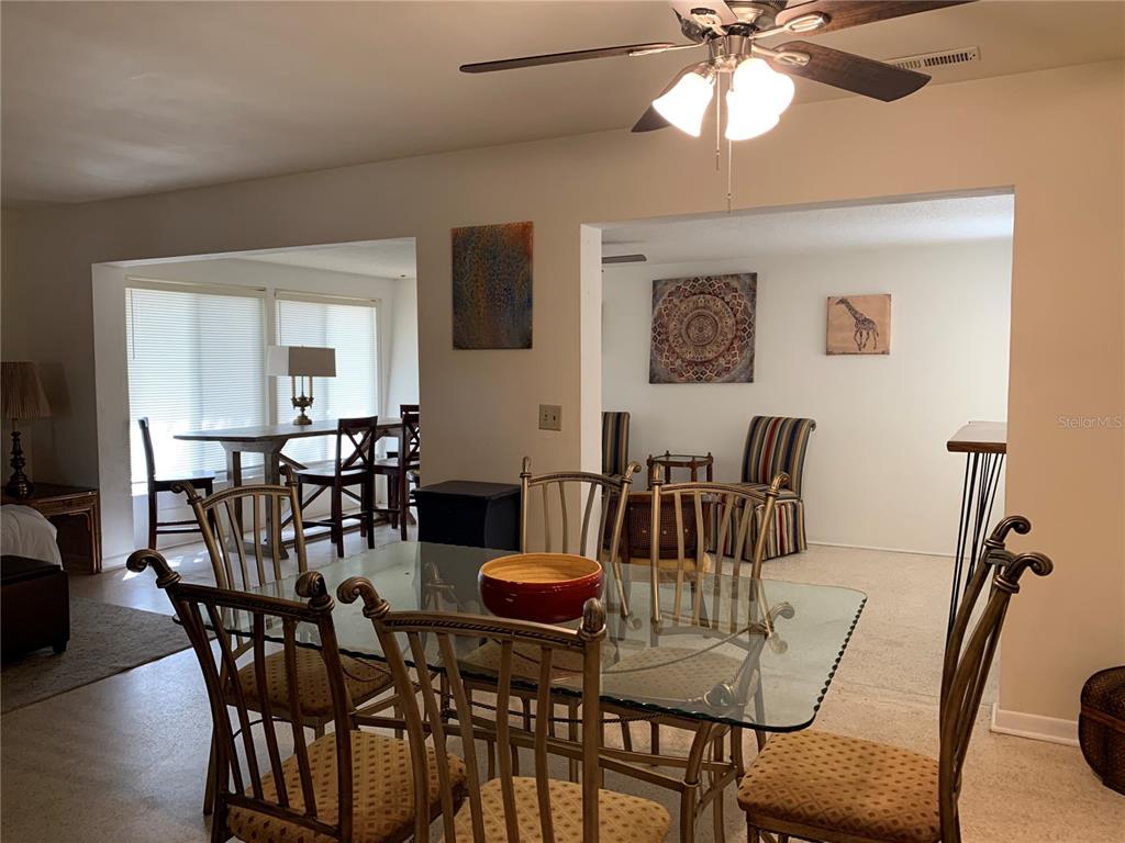 A dining room with a glass-topped table and metal chairs sits before an open living area — 1750 DRUID ROAD E, CLEARWATER, FL