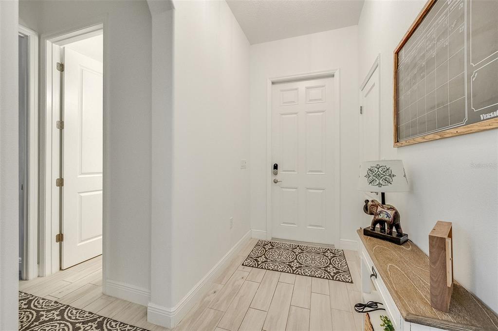 An entryway features light-colored tile flooring, white walls, a white front door, and a console table — 8048 GULLEN DRIVE, MELBOURNE, FL