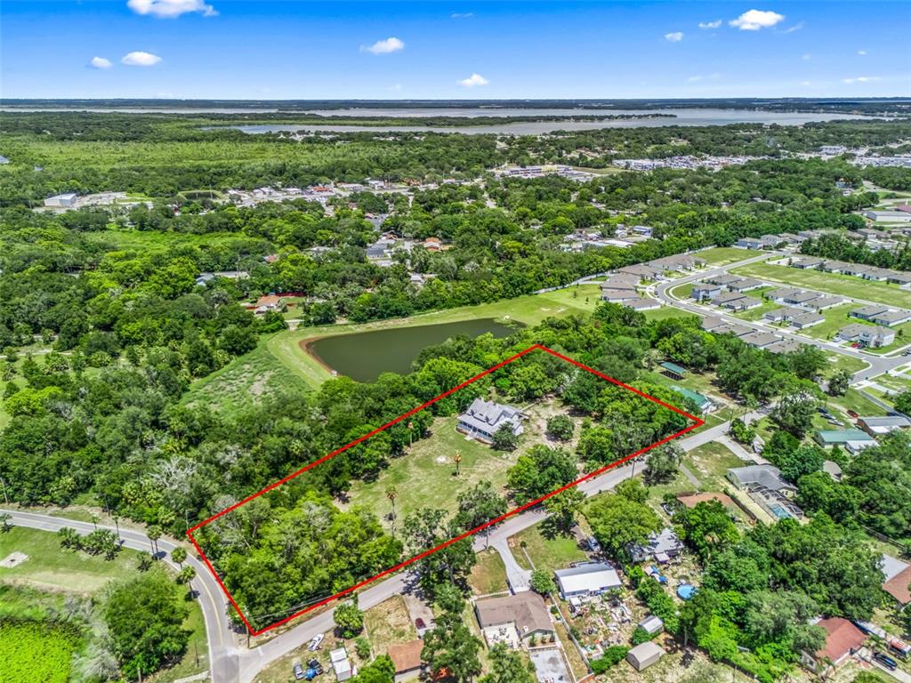 An aerial view shows a house situated on a large, tree-filled lot outlined in red — 511 E MIRROR LAKE DRIVE, FRUITLAND PARK, FL