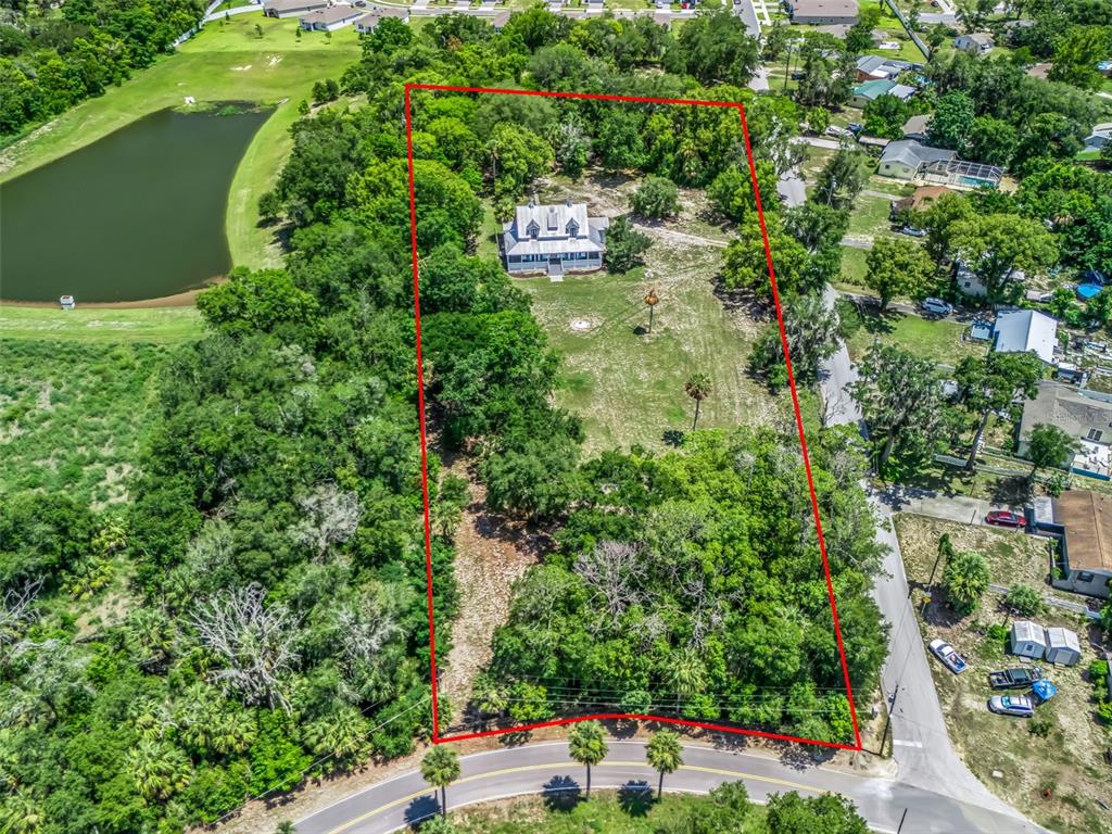 An aerial view shows a house situated on a large, tree-lined lot with a pond — 511 E MIRROR LAKE DRIVE, FRUITLAND PARK, FL