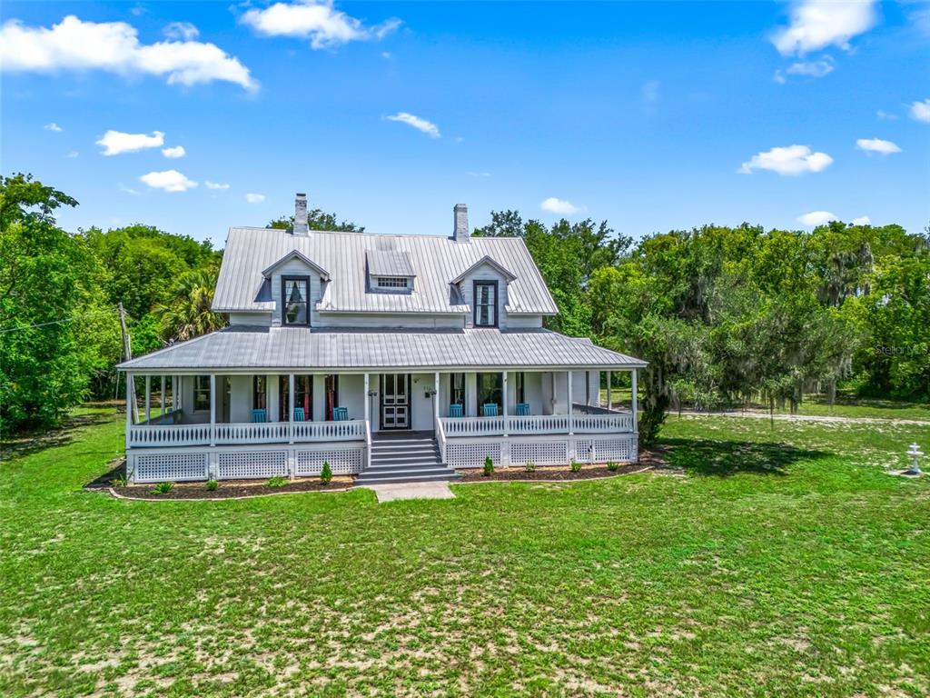 A white two-story farmhouse with a metal roof and a wrap-around porch sits on grass — 511 E MIRROR LAKE DRIVE, FRUITLAND PARK, FL
