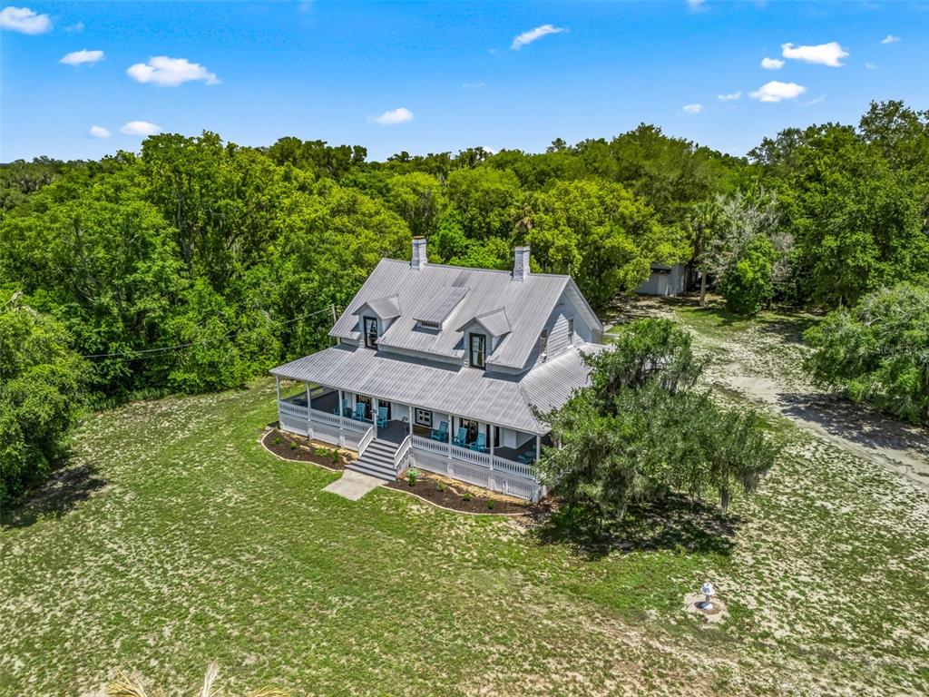 An aerial view shows a two-story farmhouse with a metal roof and a wrap-around porch — 511 E MIRROR LAKE DRIVE, FRUITLAND PARK, FL