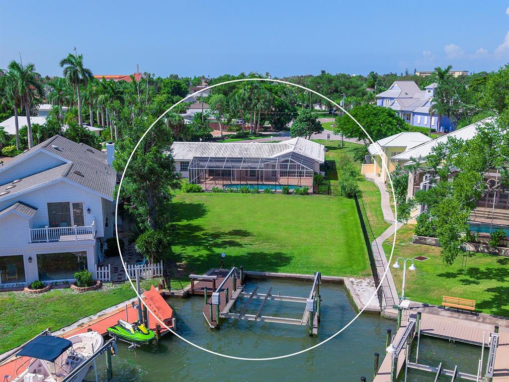 An aerial view shows a waterfront house with a pool cage, lawn, and boat lift — 396 BAYSHORE DRIVE, VENICE, FL