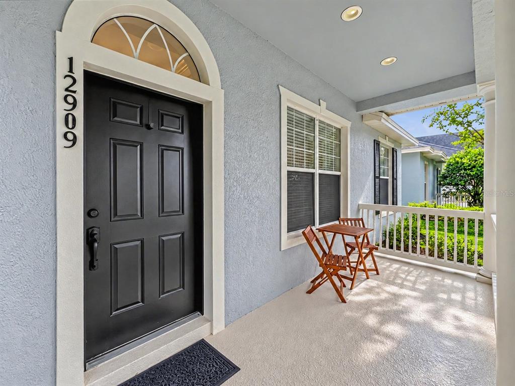 A covered front porch features a black door, a small wooden table, and two chairs — 12909 CRAGSIDE LANE, WINDERMERE, FL