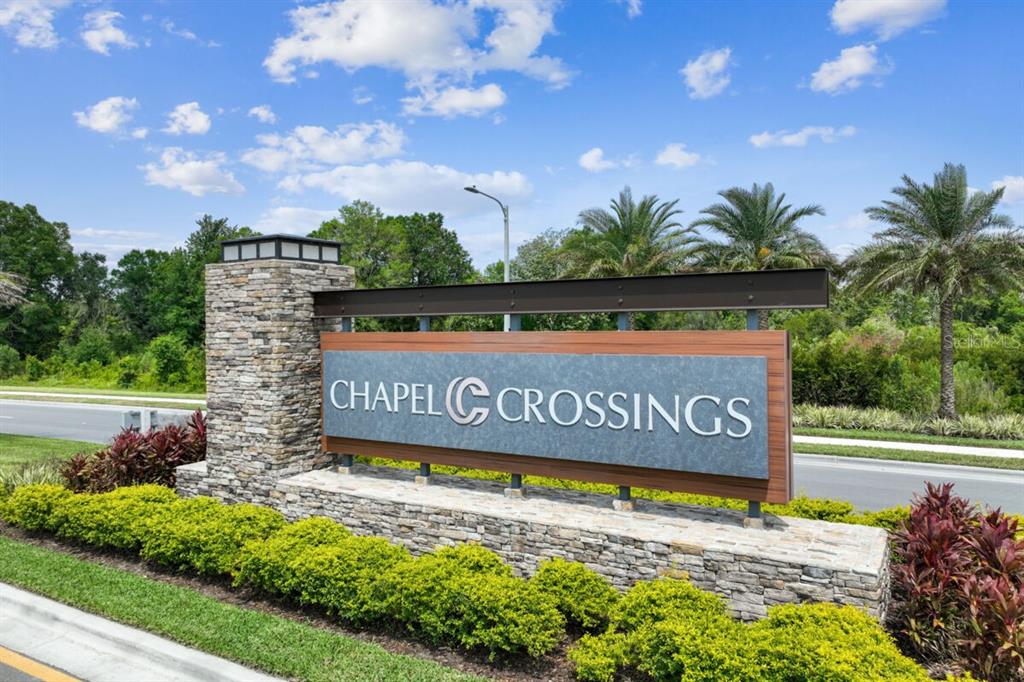 A stone and metal monument sign for Chapel Crossings stands beside a road with landscaping — 5663 MAYDALE AVENUE, WESLEY CHAPEL, FL