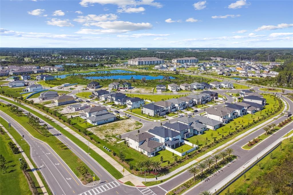 An aerial view of a suburban neighborhood featuring single-family homes, roads, and a central pond — 5663 MAYDALE AVENUE, WESLEY CHAPEL, FL