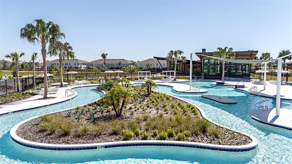 A resort-style swimming pool features a central landscaped island and a surrounding lazy river — 5663 MAYDALE AVENUE, WESLEY CHAPEL, FL