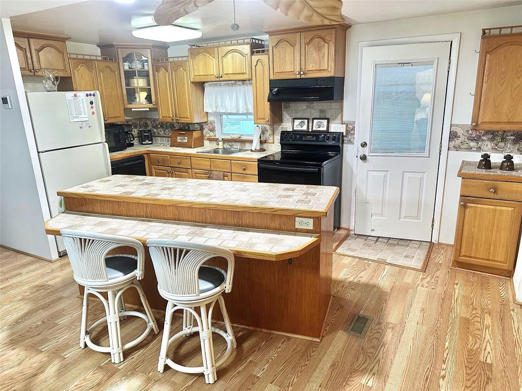 A kitchen features light wood cabinets, a tiled island with two chairs, and laminate flooring — 11211 101ST STREET UNIT 93, LARGO, FL