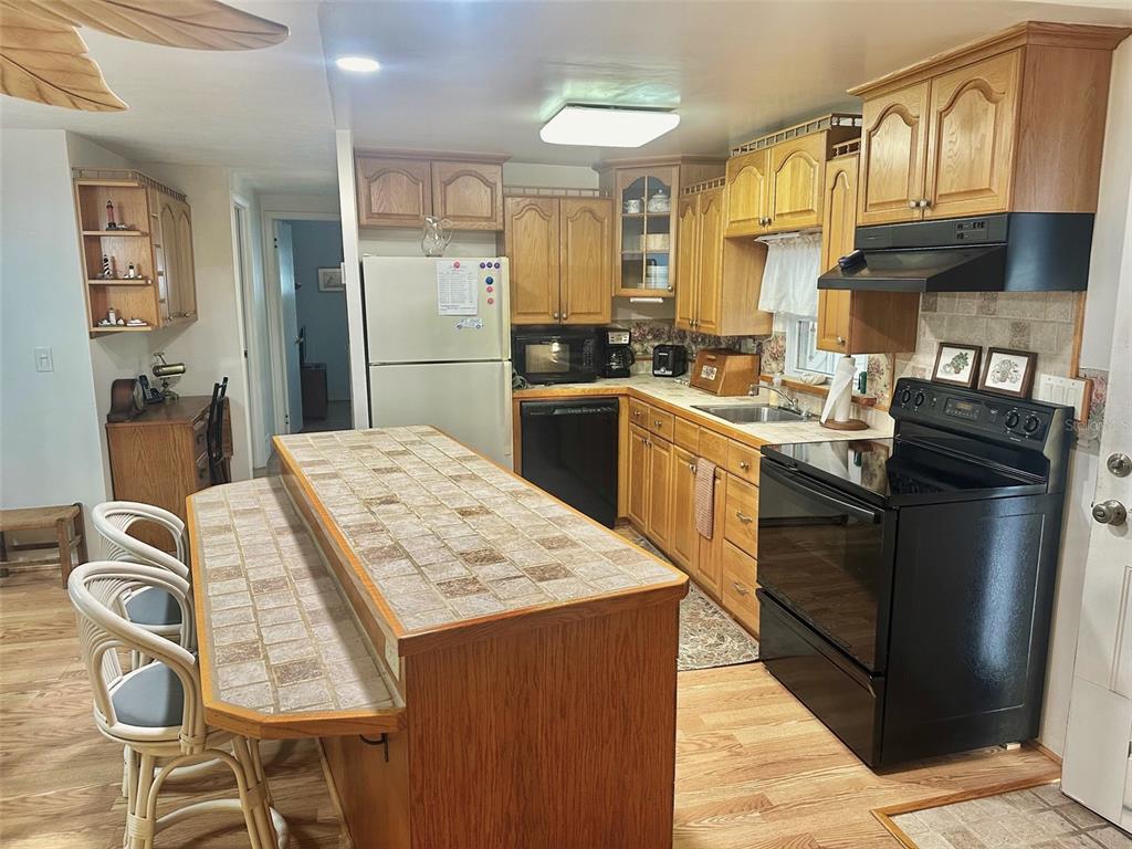 A kitchen features oak cabinets, black appliances, a tiled island, and light wood-look flooring — 11211 101ST STREET UNIT 93, LARGO, FL