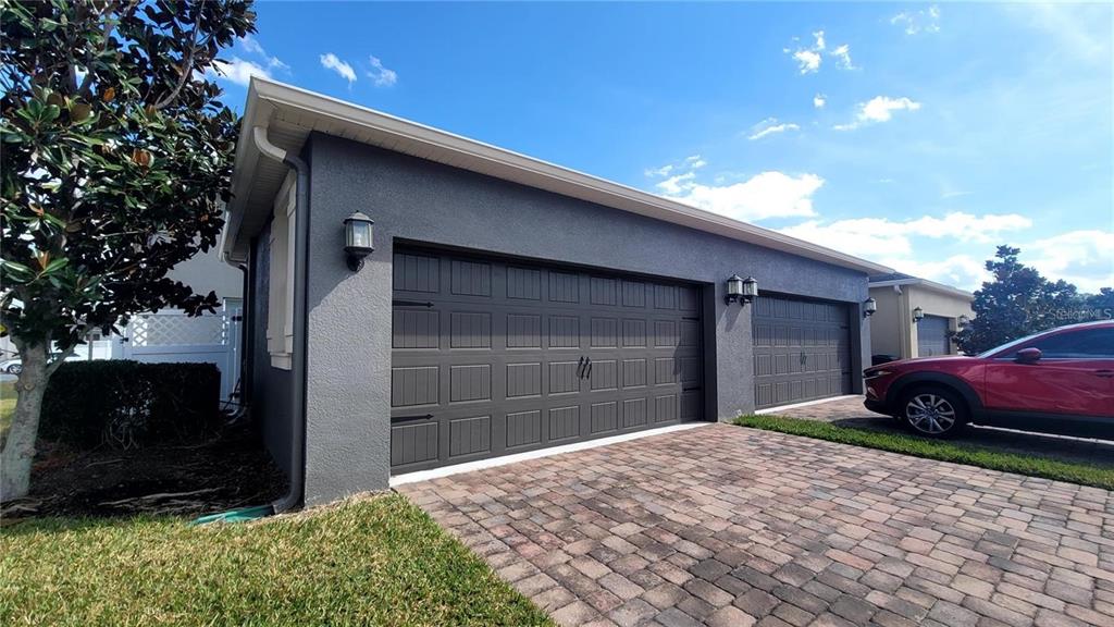 A gray detached garage with two dark doors and a brick paver driveway — 7612 FAIRGROVE AVENUE, WINDERMERE, FL