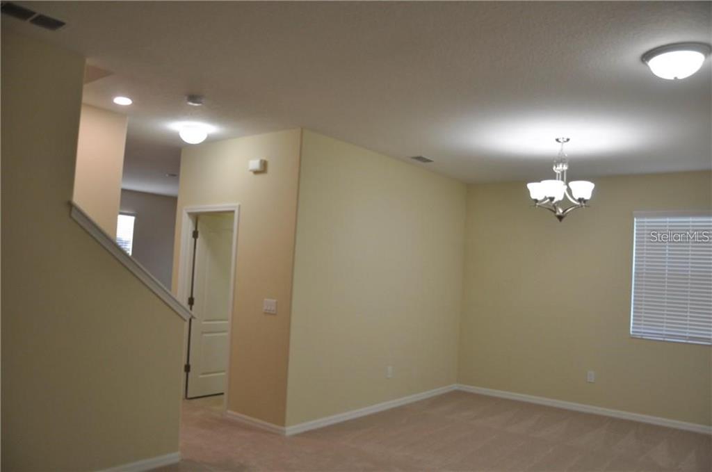 A carpeted room with a chandelier, a staircase, and a doorway leading to another area — 7612 FAIRGROVE AVENUE, WINDERMERE, FL