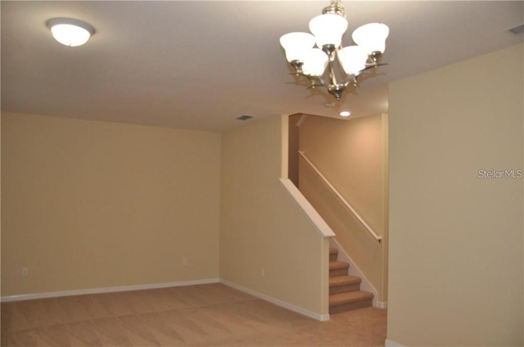 A carpeted room features a staircase with a white railing and a multi-light chandelier — 7612 FAIRGROVE AVENUE, WINDERMERE, FL