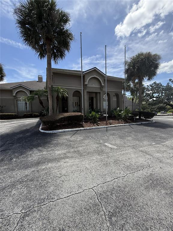 The exterior of a beige building features arched entryways, three flagpoles, and surrounding palm trees — 305 WYMORE ROAD UNIT # 107, ALTAMONTE SPRINGS, FL