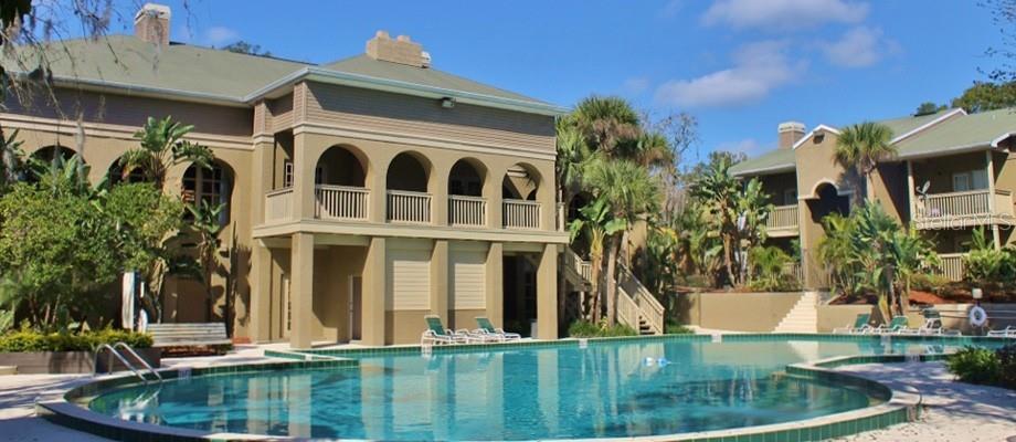 A swimming pool sits in front of a multi-story building with arched balconies and palm trees — 305 WYMORE ROAD UNIT # 107, ALTAMONTE SPRINGS, FL