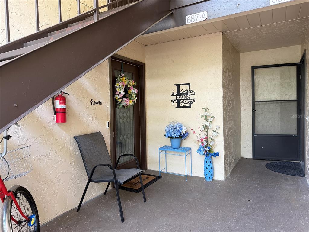 An outdoor entryway features a staircase, a front door with a wreath, and patio furniture — 687 MIDWAY DRIVE UNIT A, OCALA, FL