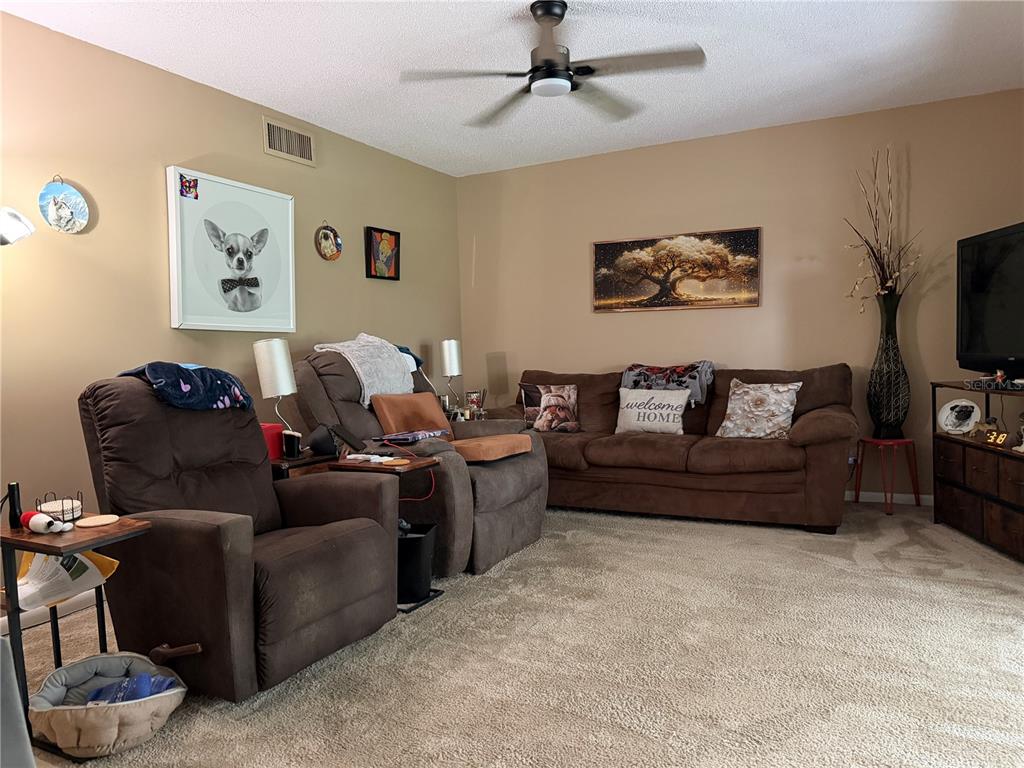 A living room features brown sofas, a ceiling fan, and wall art on tan walls — 687 MIDWAY DRIVE UNIT A, OCALA, FL