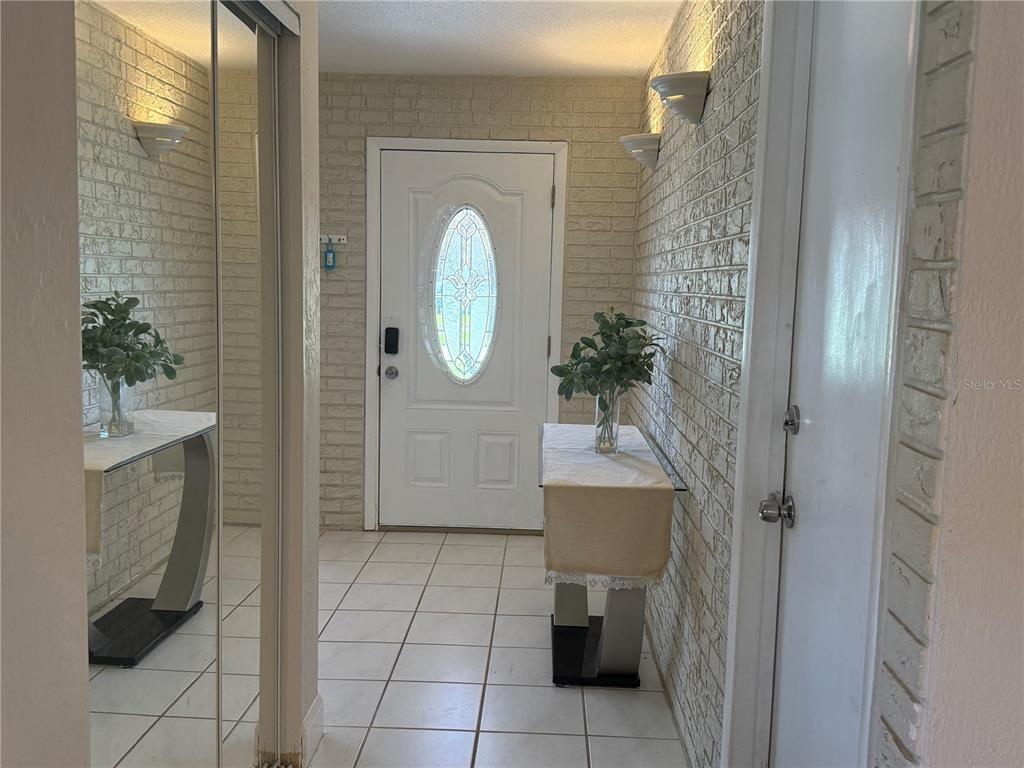 An entryway features white brick walls, tiled floors, a front door, and two mirrored consoles — 409 NEEDLES DRIVE, PORT ORANGE, FL