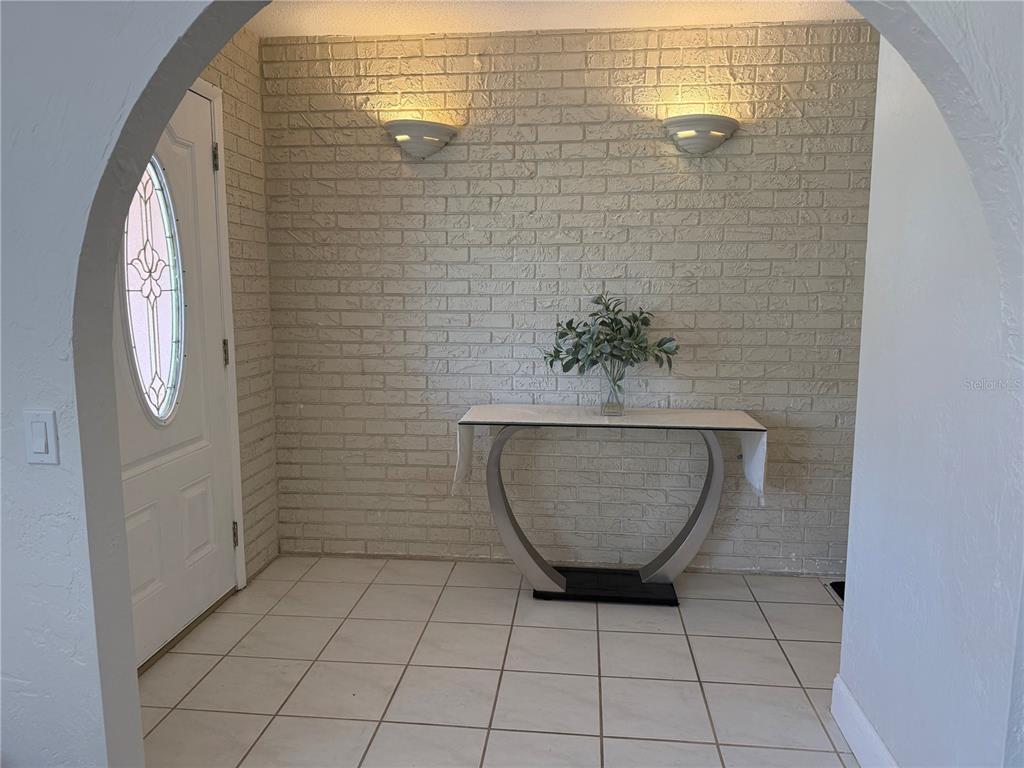 An entryway features a white brick wall, tiled floor, arched doorway, and a modern console table — 409 NEEDLES DRIVE, PORT ORANGE, FL