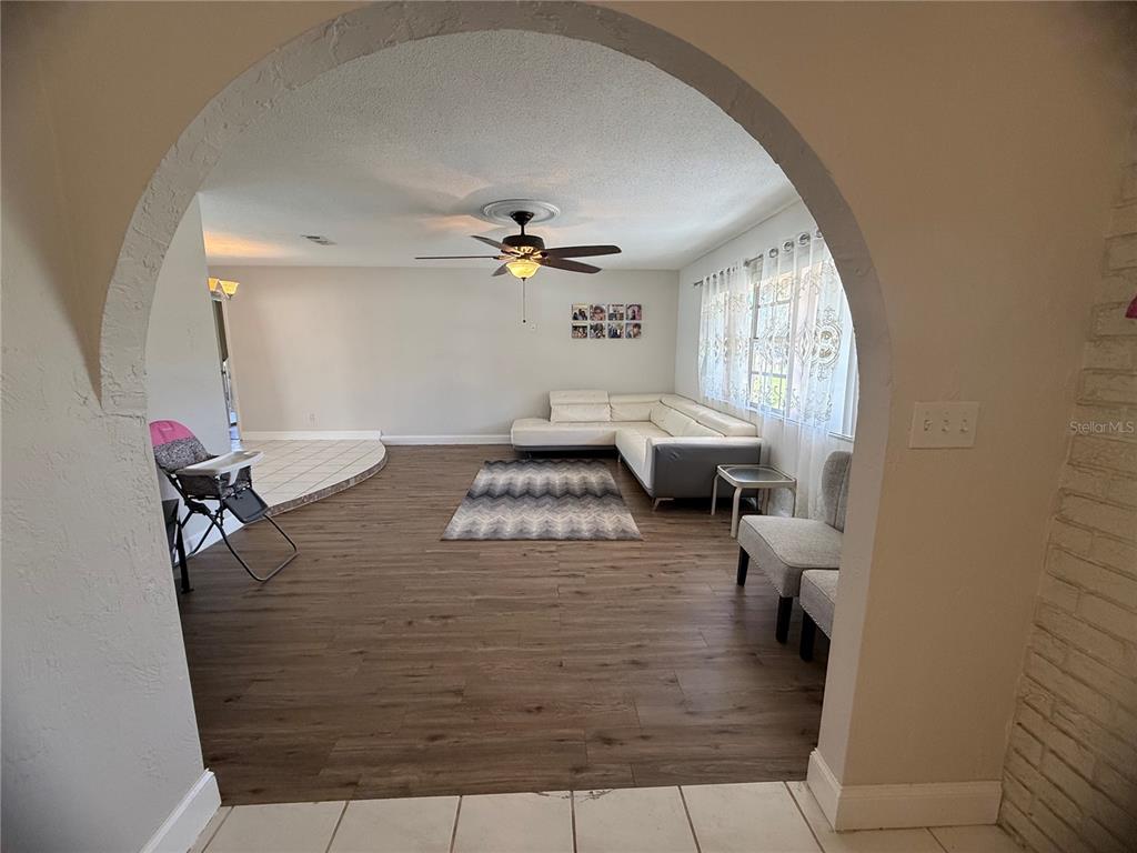 A living room features wood-look flooring, a white sectional sofa, and an arched entryway — 409 NEEDLES DRIVE, PORT ORANGE, FL