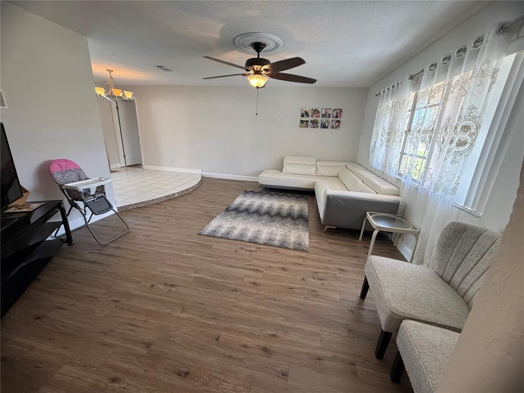 A living room features wood-look flooring, a white sectional sofa, and a ceiling fan — 409 NEEDLES DRIVE, PORT ORANGE, FL