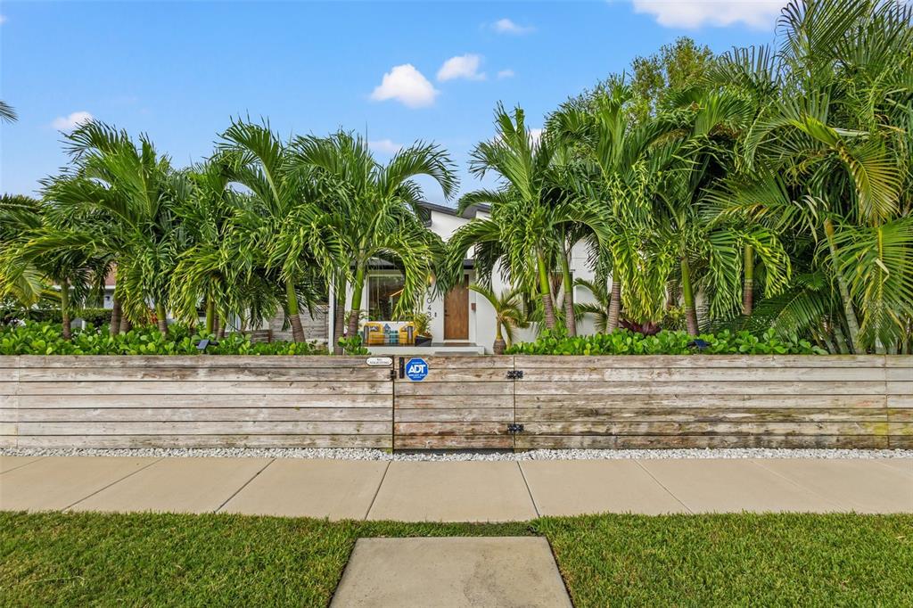 A modern white house is partially obscured by palm trees behind a horizontal wood fence — 4043 7TH AVENUE N, ST PETERSBURG, FL