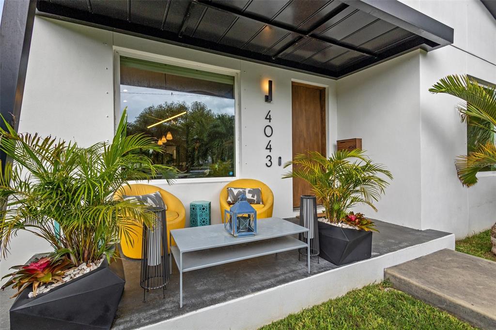 A modern front porch features two yellow chairs, a gray table, and potted palm plants — 4043 7TH AVENUE N, ST PETERSBURG, FL