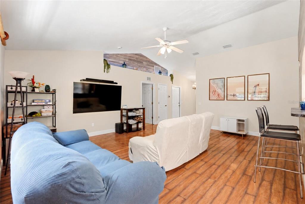 A living room features wood-look flooring, a vaulted ceiling, and a wood-paneled accent wall — 17686 NW 239TH TERRACE, HIGH SPRINGS, FL