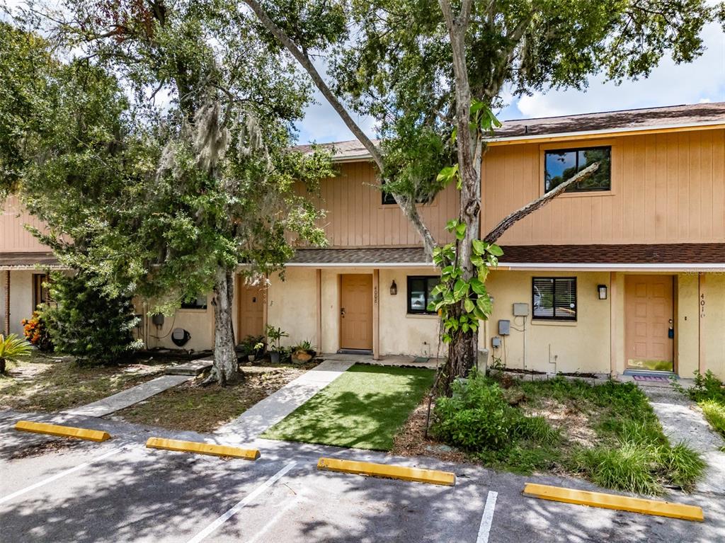 A two-story townhouse exterior with tan siding, a parking lot, and mature trees — 4008 OAK LIMB, TAMPA, FL