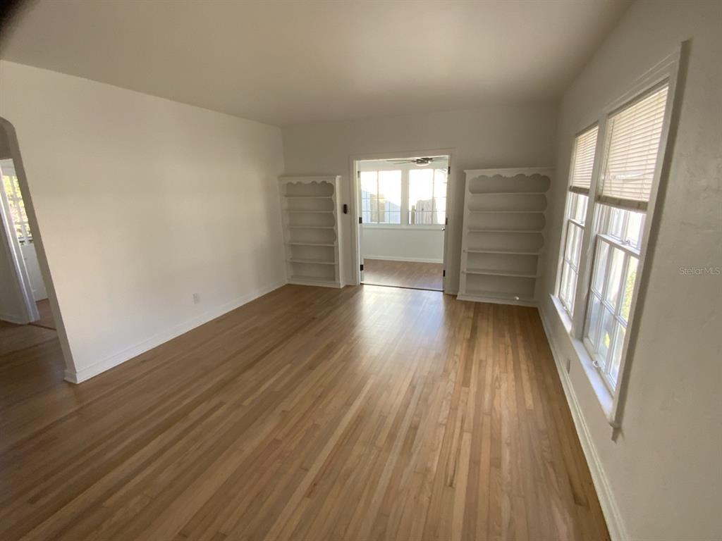 A living room with hardwood floors, white walls, built-in shelving, and a doorway to a sunroom — 608 HIGHLAND AVENUE, ORLANDO, FL