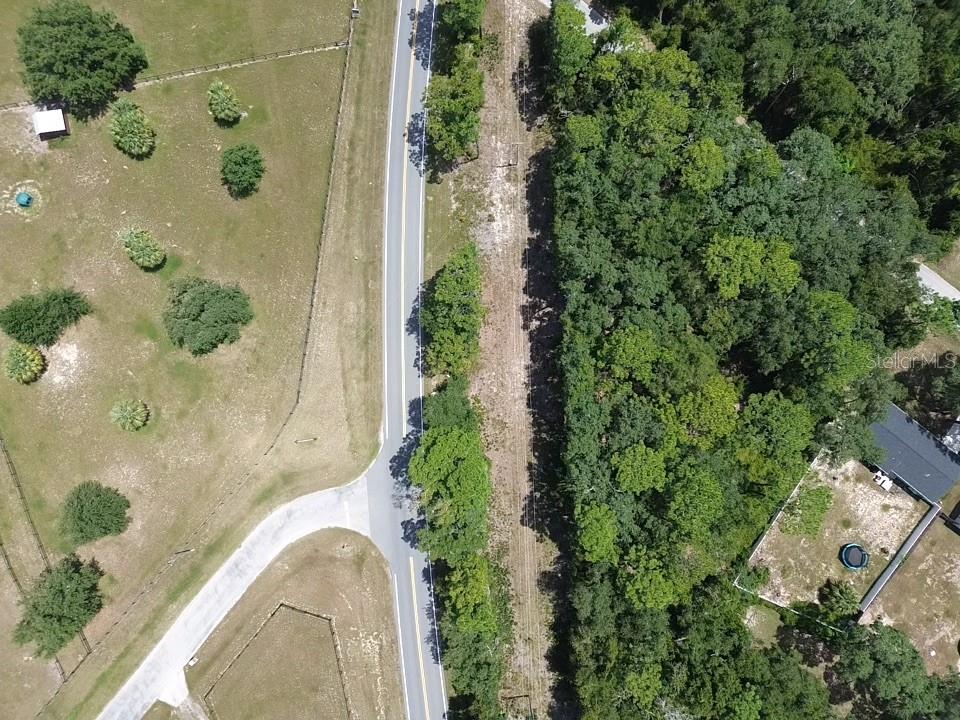 An aerial view shows a paved road running between a grassy field and a wooded area — TBD SE 180TH AVE ROAD, OCKLAWAHA, FL