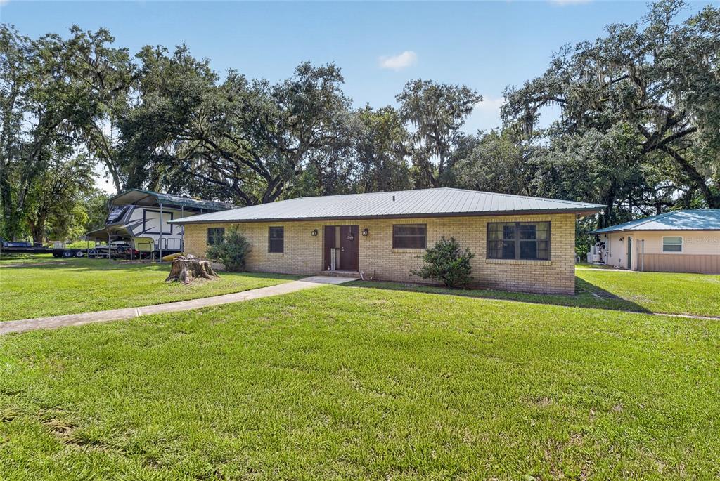 A single-story brick house with a metal roof sits on a grassy lot with trees — 7468 CR 650, BUSHNELL, FL