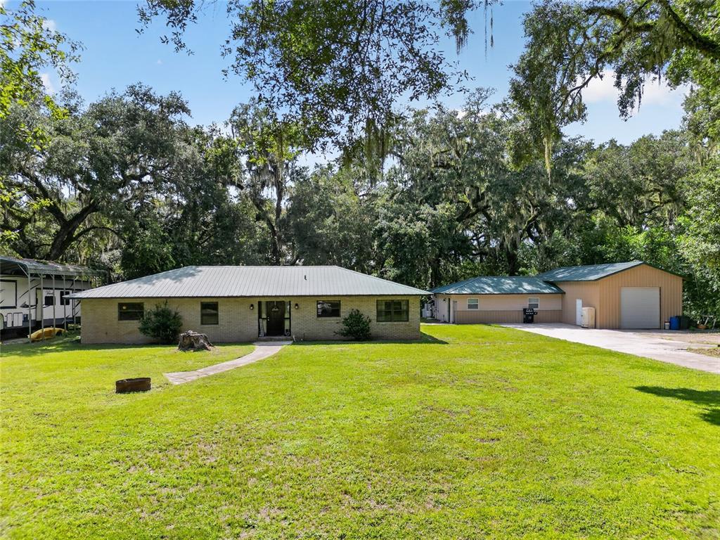 A single-story brick house with a metal roof and a detached garage on a lawn — 7468 CR 650, BUSHNELL, FL