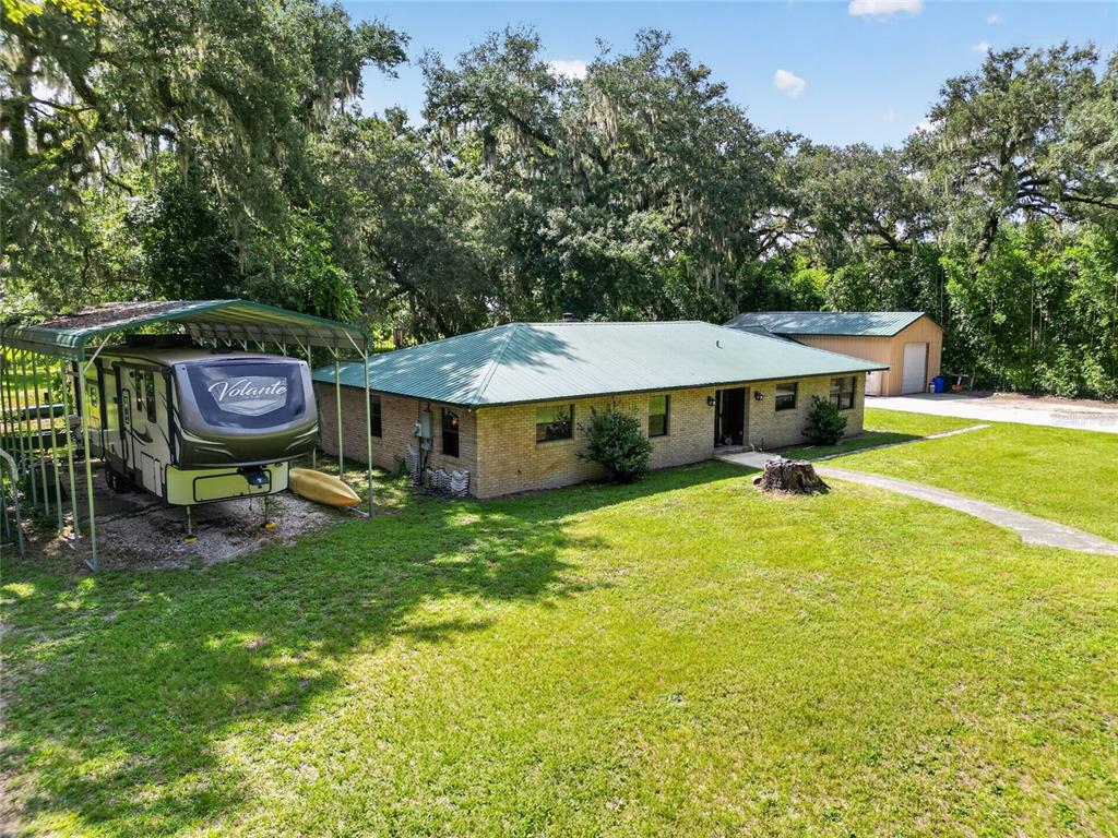 A brick house with a green metal roof sits next to a covered RV shelter — 7468 CR 650, BUSHNELL, FL
