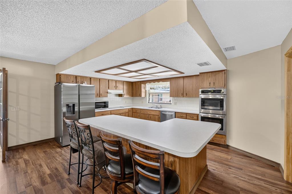 A kitchen with wood cabinets, stainless steel appliances, a white island, and wood-look flooring — 7468 CR 650, BUSHNELL, FL
