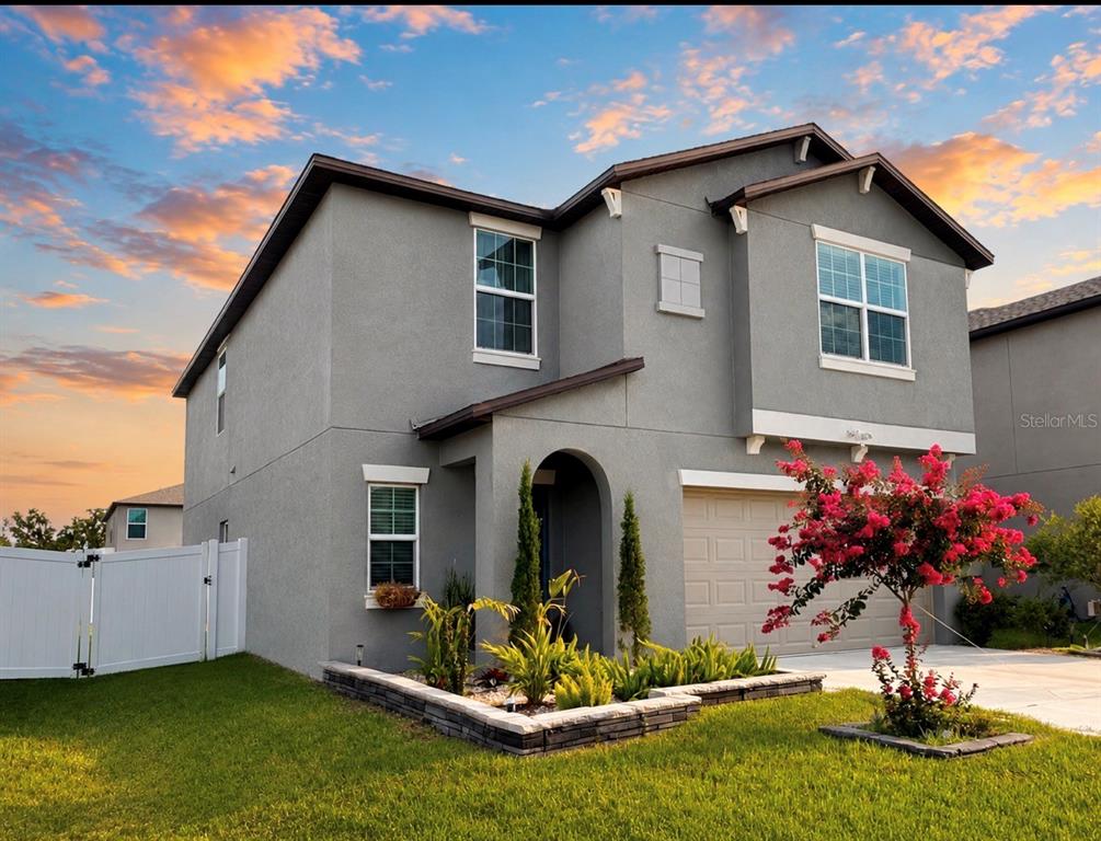 A two-story gray stucco house with a front garden and a white vinyl fence — 6470 BACK FORTY LOOP, ZEPHYRHILLS, FL