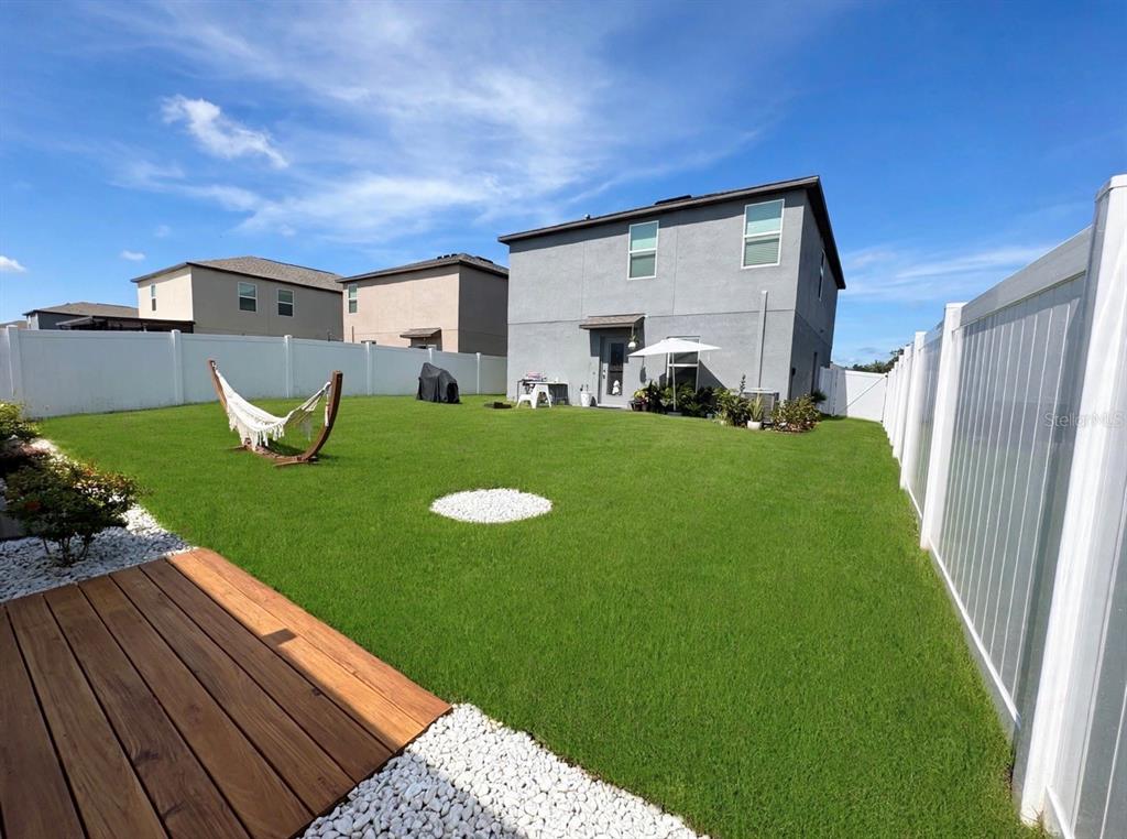 A backyard features a wooden deck, a hammock, a white vinyl fence, and a two-story house — 6470 BACK FORTY LOOP, ZEPHYRHILLS, FL