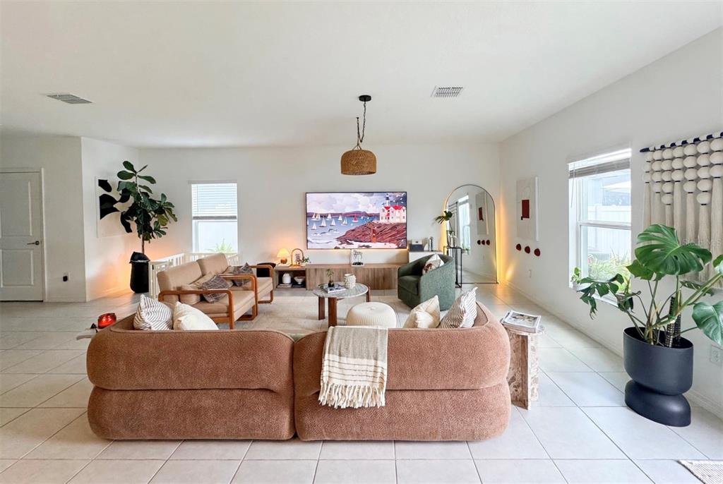 A living room features a large brown sectional sofa, a television, and several potted plants — 6470 BACK FORTY LOOP, ZEPHYRHILLS, FL